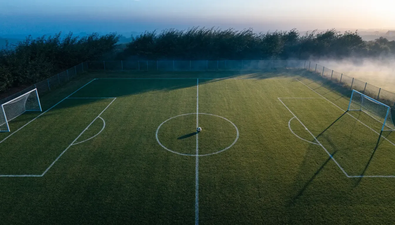 Ein Fussballplatz von oben gesehen, die Linien bilden ein helles Muster auf dem Rasen, Drohnenperspektive in der Morgendämmerung.