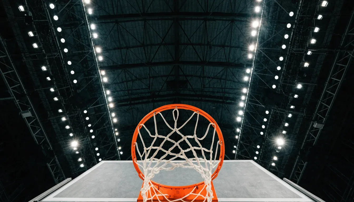 Ein Basketballkorb von unten gesehen, darüber eine Hallendecke mit Scheinwerfern und Stahlträgern.