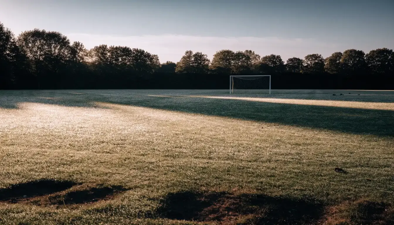 Ein Fussballtor mit Netz in der Totalen auf einem leeren Platz, Tau glänzt im Gras und die Morgensonne steht tief.
