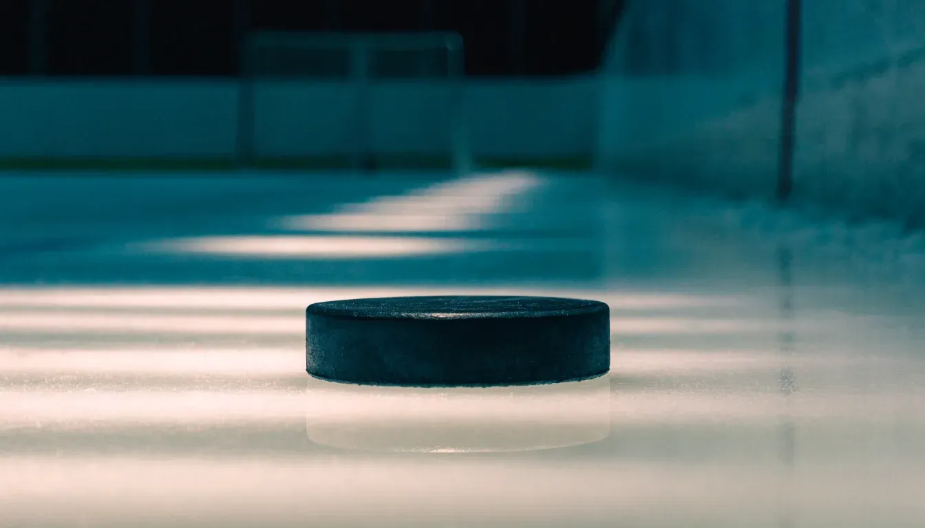 Ein Eishockeypuck liegt in Grossaufnahme auf glatter Eisfläche, im Eis spiegeln sich Hallenlichter.